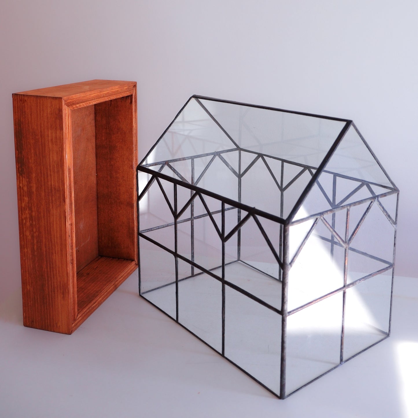 A large hand soldered terrarium sitting next to its wooden base.