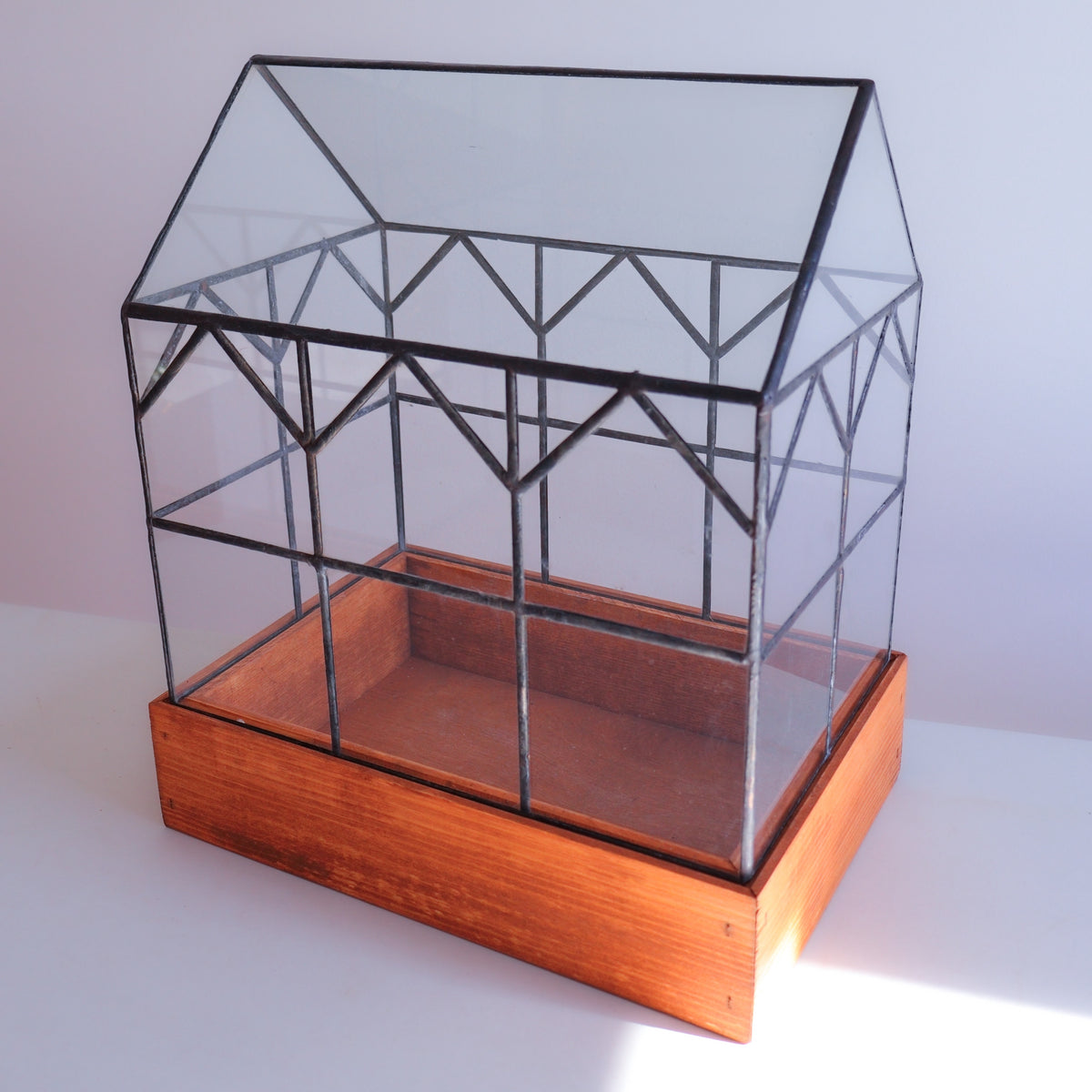 An empty stained glass terrarium made of glass and solder on a warm colored wooden base