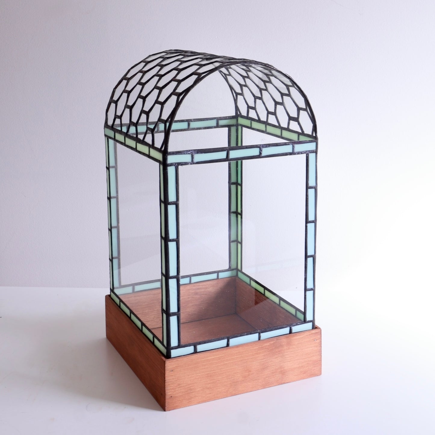 Stained glass display case with honeycomb curved top on wooden base on a white background