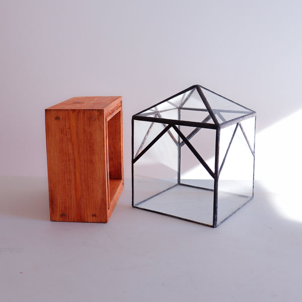 A handcrafted stained glass terrarium sitting next to its handmade wood base. 