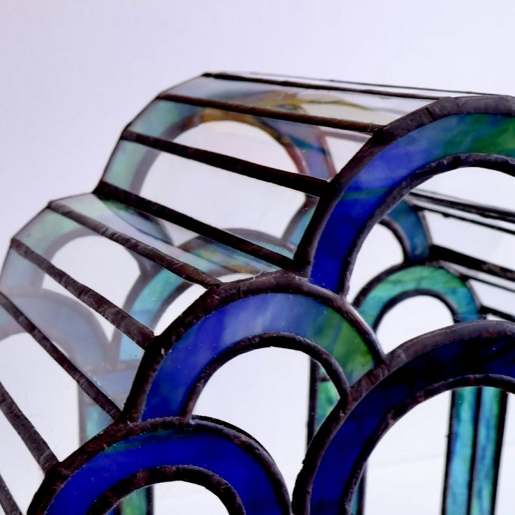 Close-up of a stained glass terrarium with blue and green colors on a light gray background