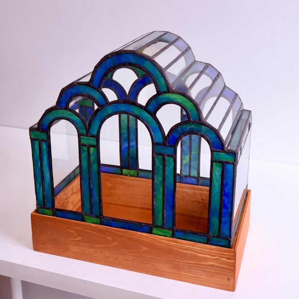 Stained glass terrarium with blue and green glass on a wooden base. 