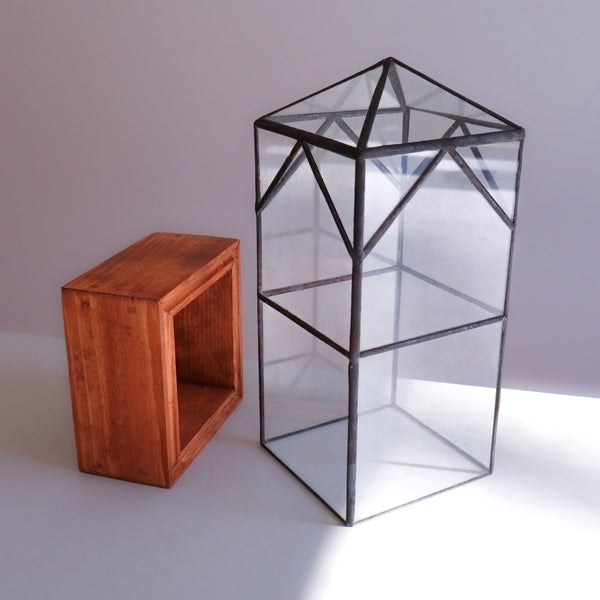 A large glass terrarium for plants lifted off of its handmade wood base. 